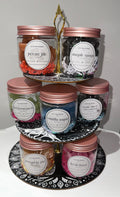 JuJu's Meltdowns wax melt jars displayed on a tiered stand with rose gold lids and handwritten scent labels