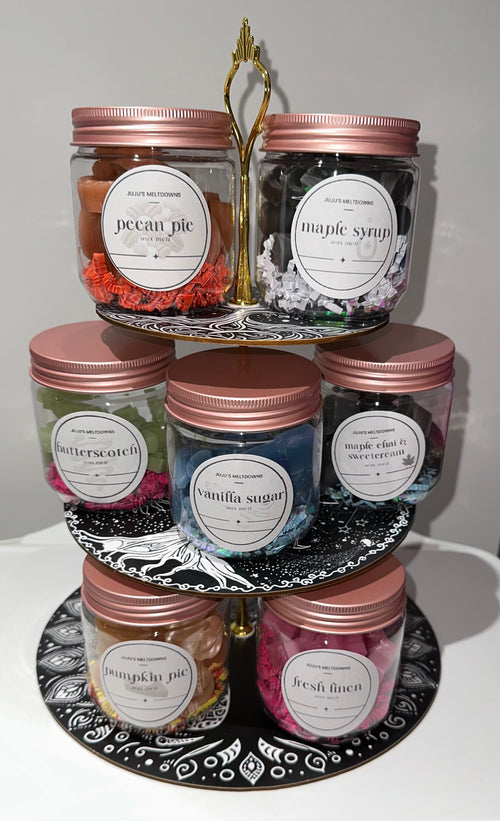 JuJu's Meltdowns wax melt jars displayed on a tiered stand with rose gold lids and handwritten scent labels